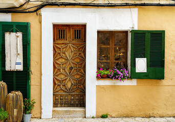 Fototapeta na wymiar Beautiful house facade with an impressive wooden door and window shutters with blank signs for decoration. Mediterranean summer travel background with text space.