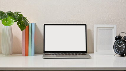 Obraz premium Mock up of creative workspace with laptop, vase, frame, clock, and books on white table. Blank screen laptop.