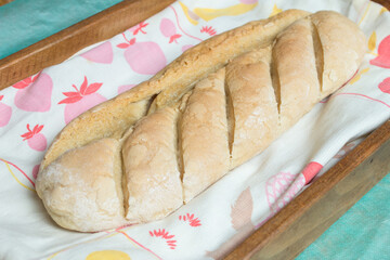 A loaf of homemade bread on a cloth decorated with fruits inside a wooden tray in the kitchen. Steps to make bread at home.