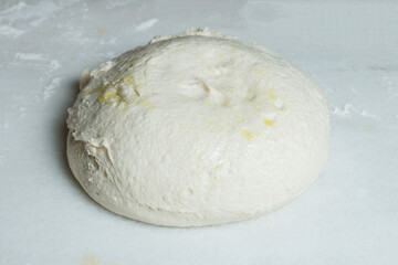 Spongy homemade bread dough with olive oil from the first fermentation on a marble table. Steps to make bread at home.