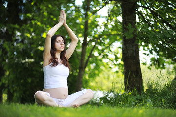 Naklejka na ściany i meble Pregnant woman doing yoga exercise in nature on a summer