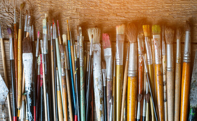 Fototapeta premium Mixed painting brushes lying on the wooden background. Toned image.