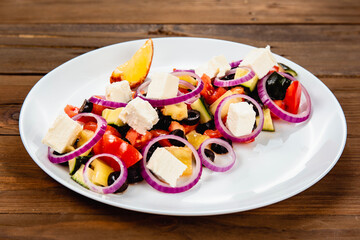 Greek salad, dressed with olive oil on a white plate on a wooden background