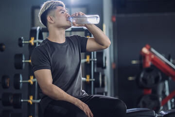 Sportsman drinking water in fitness gym having break after doing exercise.