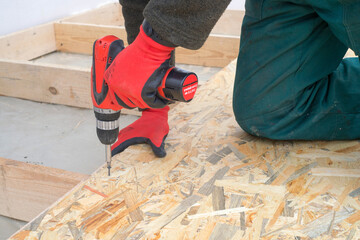 Man worker screws wooden oriented stands bords on insulated floor. New house constuction