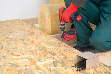 Man worker screws wooden oriented stands bords on insulated floor. New house constuction