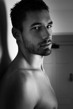 Portrait of handsome shirtless man looking at camera against white wall.