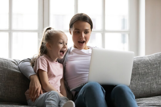 Happy young mother and little schoolgirl daughter looking at laptop screen, amazed by good discounts sale offers in internet store, involved in online shopping, surprised family watching funny movie.