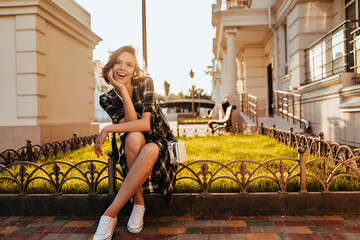 Adorable white girl in gumshoes posing in sunny autumn day. Outdoor photo of stylish jocund female...
