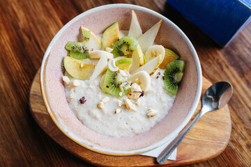 Oatmeal with fruits and nuts served in a bowl on a board with a teaspoon