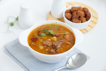 Pea soup with meat, smoked sausage, pea sprouts and croutons. Traditional Russian dish. Home kitchen. Close-up, selective focus.
