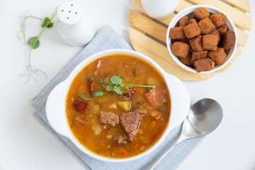 Pea soup with meat, smoked sausage, pea sprouts and croutons. Traditional Russian dish. Home kitchen. Close-up, selective focus.