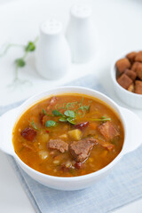 Pea soup with meat, smoked sausage, pea sprouts and croutons. Traditional Russian dish. Home kitchen. Close-up, selective focus.