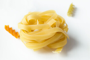 tagliatelle pasta on a white table, next to colored pasta