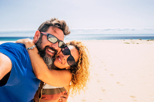 happy and healthy couple of people enjoying their life and their vacations outdoors at the beach together taking a selfie with the sea or ocean in  background - two happy people taking a picture 
