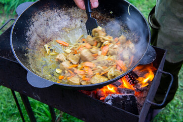 Cooking food on an open fire in a cauldron. The hand of the chef mixes meat and vegetables with a spatula