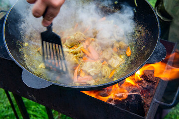 Cooking food on an open fire in a cauldron. The hand of the chef mixes meat and vegetables with a spatula