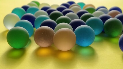 Blue and green glass frosted balls on a yellow surface. Partially defocused. Tactile play or...