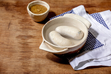 Munich Bavarian traditional white sausages in ceramic pan served with german sweet mustard on white and blue napkin over wooden background.