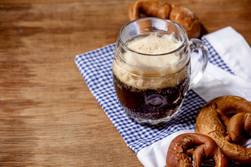 Glass of lager beer with traditional salted pretzels on white and blue napkin over wooden background. Oktoberfest theme