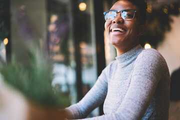 Cheerful afro american student in trendy eyewear enjoying having fun in coffee shop resting on break,happy prosperous businesswoman satisfied with successful project sitting 