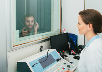 Audiologist woman doing the hearing exam to a mixed-race man patient using an audiometer in a special audio room.