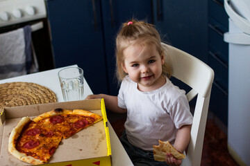 Little girl eating pizza in the kitchen at home.