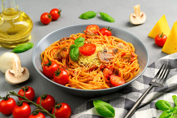 Spaghetti with tomato sauce, cherry tomatoes, mushrooms and basil in a plate on a gray background. Traditional Italian food. Close-up