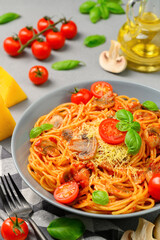 Spaghetti with tomato sauce, cherry tomatoes, mushrooms and basil in a plate on a gray background. Vertical orientation, close-up