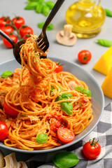 Italian pasta with tomato sauce, cherry tomatoes, mushrooms and basil on a gray concrete table. Vertical orientation.