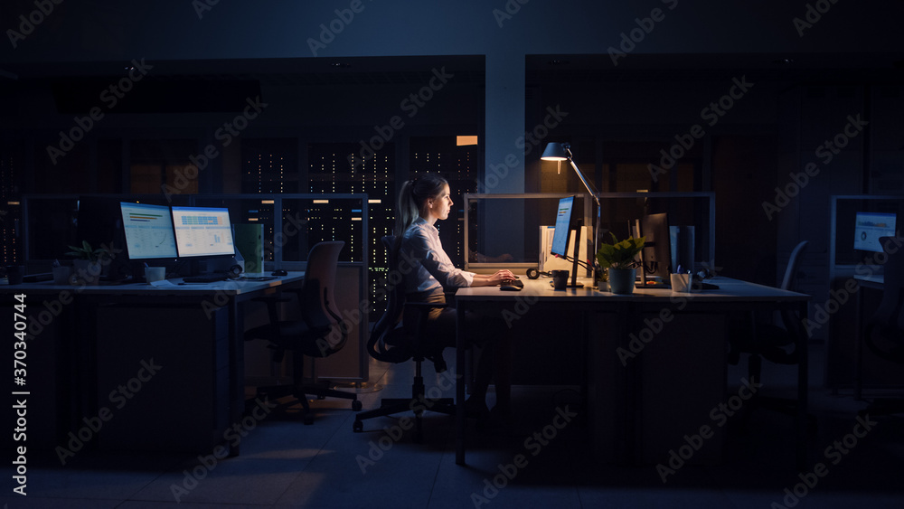 Poster working late at night in the office: businesswoman uses desktop computer, analyzing, using documents