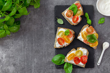 Bruschetta with dark bread, fresh juicy tomatoes, cream cheese, basil and spices on a slate base. Dark background. Top view.