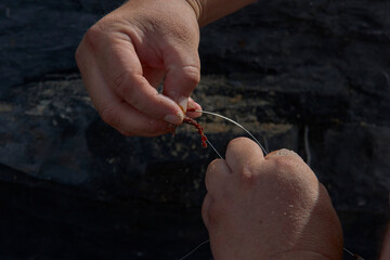 Pescador colocando un gusano como cebo en el anzuelo para pescar.