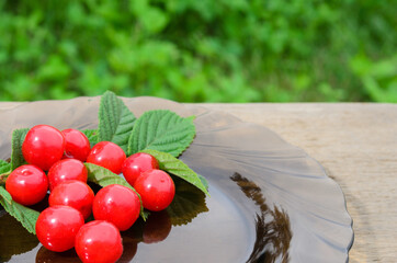 Red, ripe cherry berries with a twig and leaves on a rough wooden background.