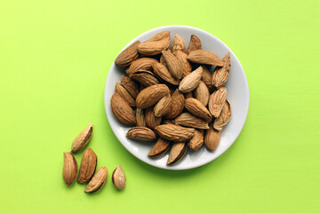 Almonds are not cleaned. Some nuts lie on a white plate in the center. Five walnuts lie separately on a yellow background. View from above. Food. Copy space. Quenching hunger. Protein. Nuts in shells.