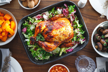 Decorated festive table with whole roasted chicken, salad, pumpkin, mushrooms, beans and walnut. The concept of family dinner or Thanksgiving celebrate