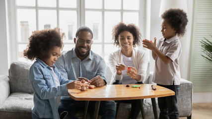Happy african American family with small kids have fun play with plasticine at home together, smiling biracial parents with children engaged in creative activity, use modeling clay, hobby concept
