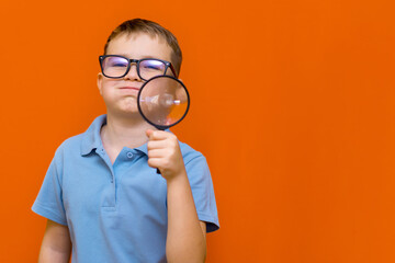 Beautiful european young boy with glasses holding and looking through magnifying glass.Orange wall.