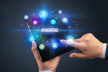 Businessman holding a foldable smartphone with #HASHTAG inscription, social media concept