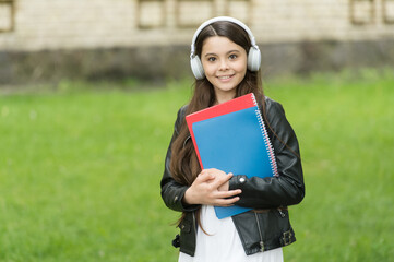 Fototapeta premium Girl listening audio carry textbooks on way to school, language lessons concept