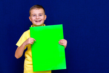 Happy calm caucasian child boy holding a poster for your information on the blue background