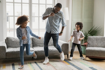 Playful young african American dad dancing playing in living room with two little children, happy biracial father have fun dancing with small kids son and daughter, enjoy weekend at home together