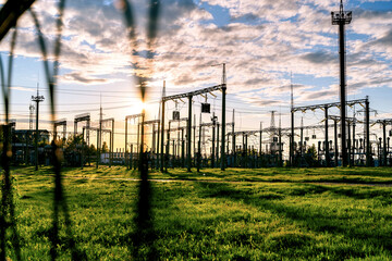 Distribution electric substation with high-voltage power lines and transformers at sunset, electric transmission tower