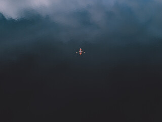Top view of a orange boat sailing in the dark blue water. Aerial view of row boat wih human hands paddling on the sea background. Copy space for text message or information content, advertise field © Claudiu