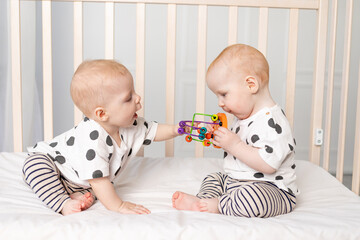two twin babies 8 months old play in the crib, early development of children up to a year, the...