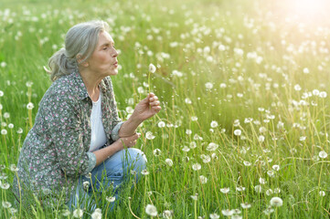 Beautiful senior woman in green field with dandelions