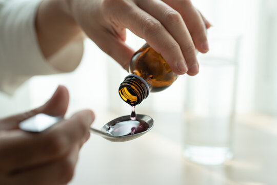 Woman hand pouring medication or cough syrup from bottle to spoon. healthcare concept