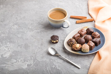 Different chocolate candies and a cup of coffee on a gray concrete background. side view, copy space.