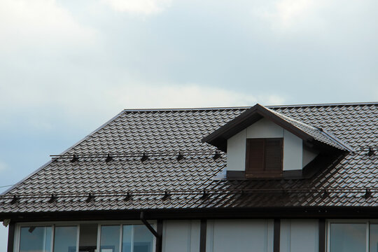 icon roof with new brown roofing tiles on residential property. banner on  roof for roofers. concept for roof housetop. roof structure with attic skylights, gutter system, windows protection and fence