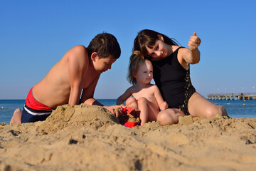 Fototapeta premium Mom, son and daughter are playing in the sand on the beach